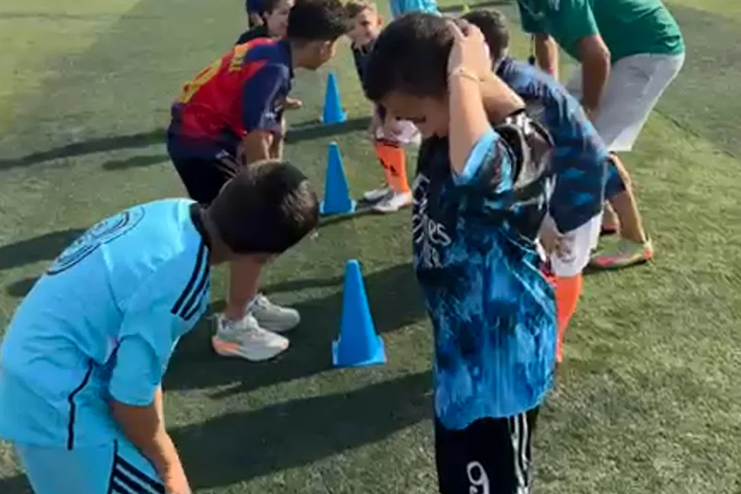 A coach and children in the academy kit gathered round a cones drill on the pitch