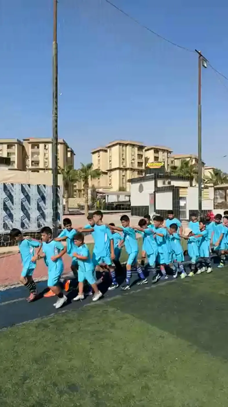 Children in the academy's sky-blue kit jogging in a line across the pitch
