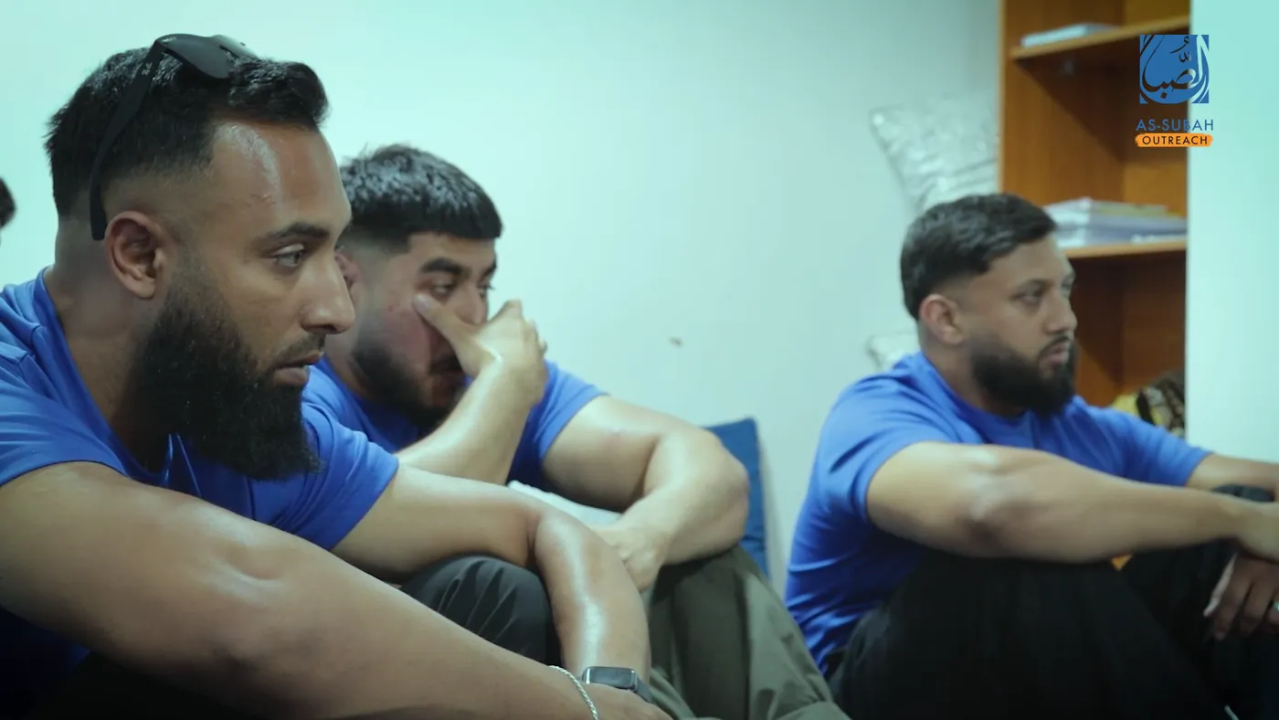Three volunteers in team shirts listening to a family, one wiping his eyes