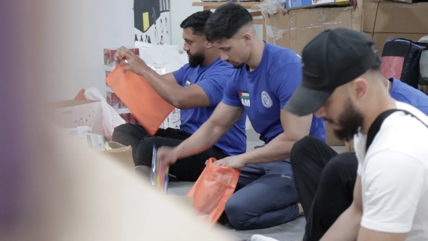 Volunteers in blue team shirts packing orange aid bags on the floor of the Cairo store room