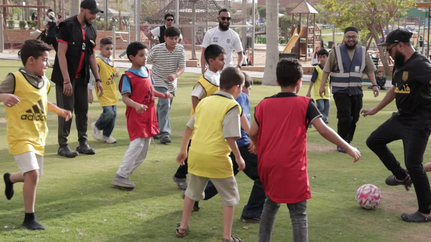 Children in red and yellow bibs playing football with volunteers in a Cairo park